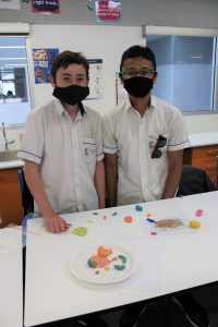 2 Year 9 students standing in front of a cell they made from coloured clay